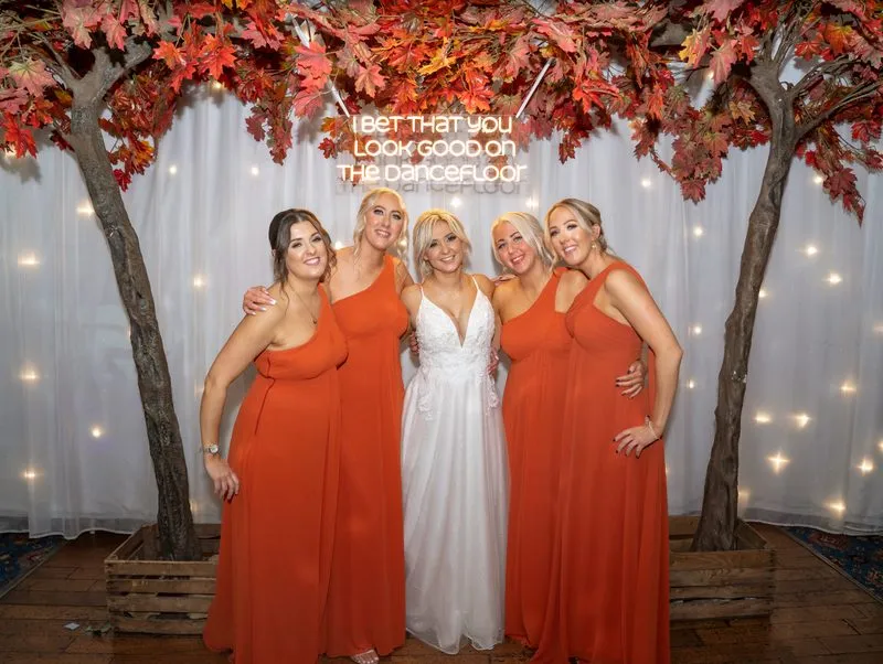 Bridesmaids in autumn colour beneath the floral arch